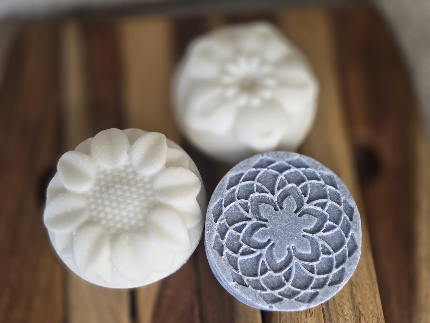 Two white flower-molded salt soap rounds with a blue mandala round behind (alternate angle)