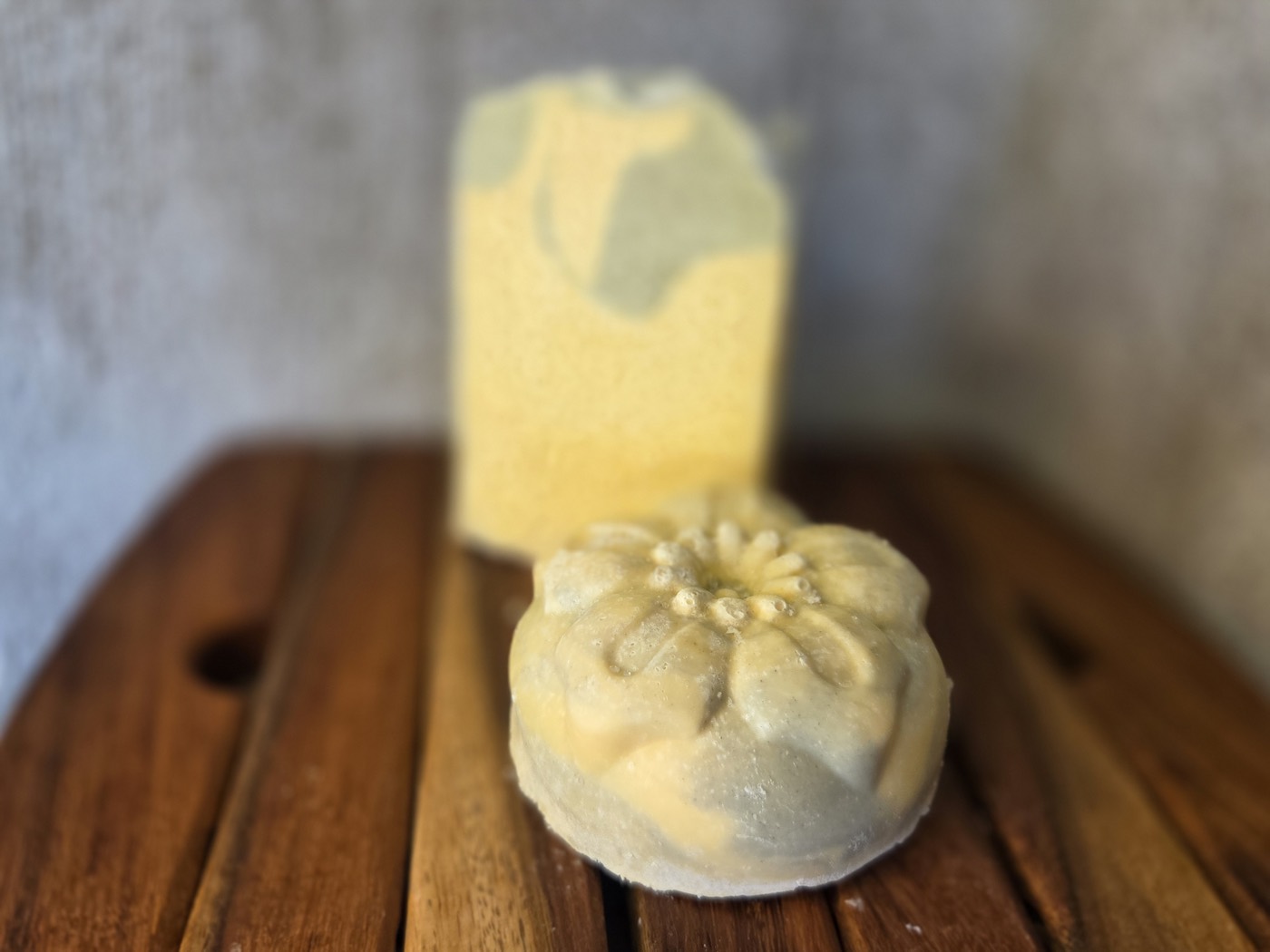 Yellow soap bar with green patches beside a green flower-molded round (alternate angle)