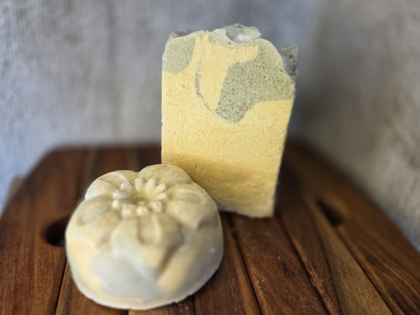 Yellow soap bar with green patches beside a green flower-molded round (alternate angle)