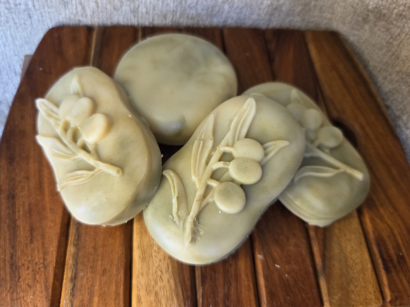 Sage-green oval guest soaps with olive-branch relief and a round puck