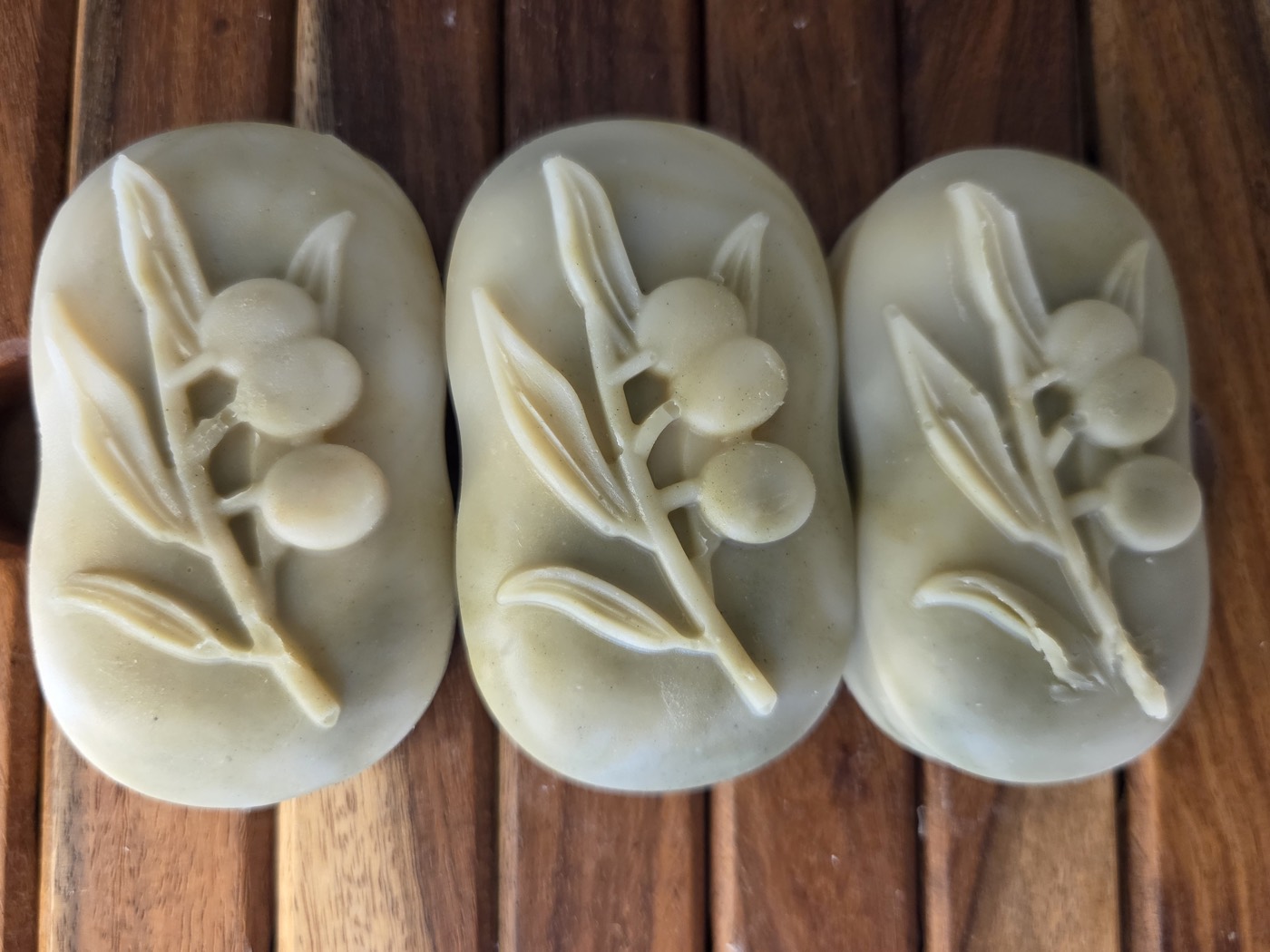 Three sage-green oval soaps with olive-branch relief, from above (alternate angle)